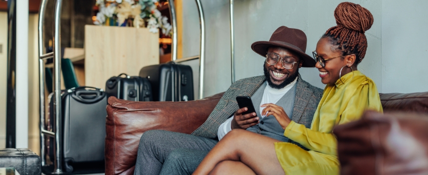 Happy black couple sitting in hotel lobby with suitcases