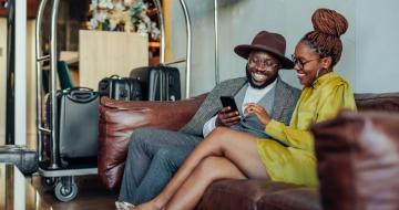 Happy black couple sitting in hotel lobby with suitcases